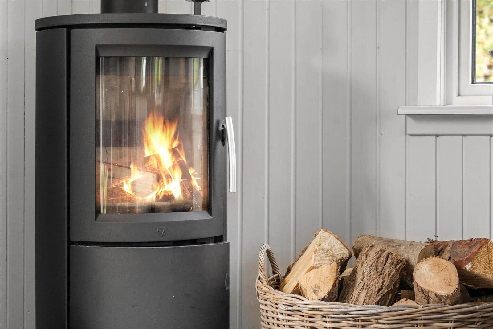 Holzofen mit brennendem Feuer und Korb mit Brennholz an der Wand.