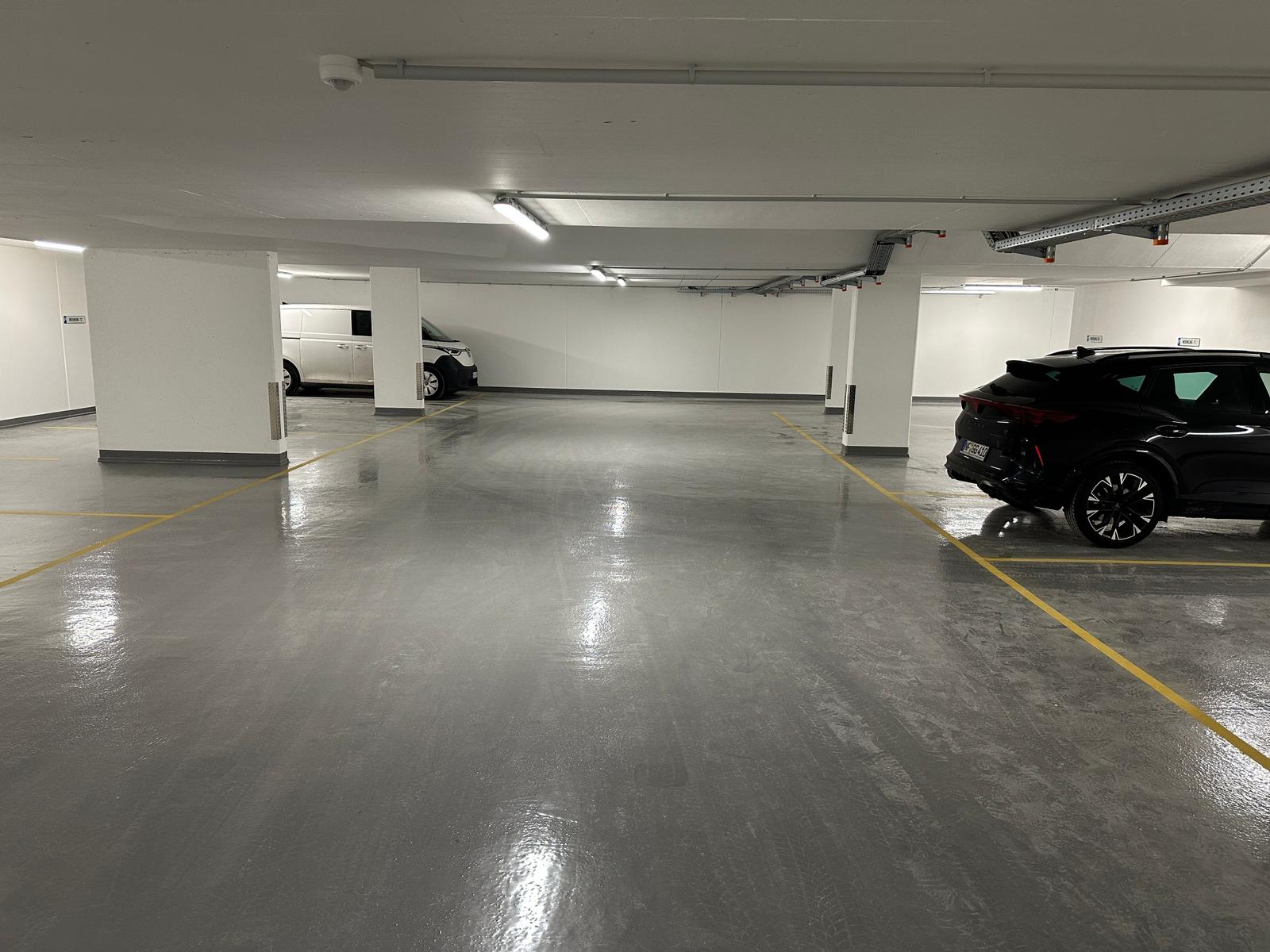 Untergeschoss-Parkhaus mit zwei geparkten Fahrzeugen und gelben Markierungen.
