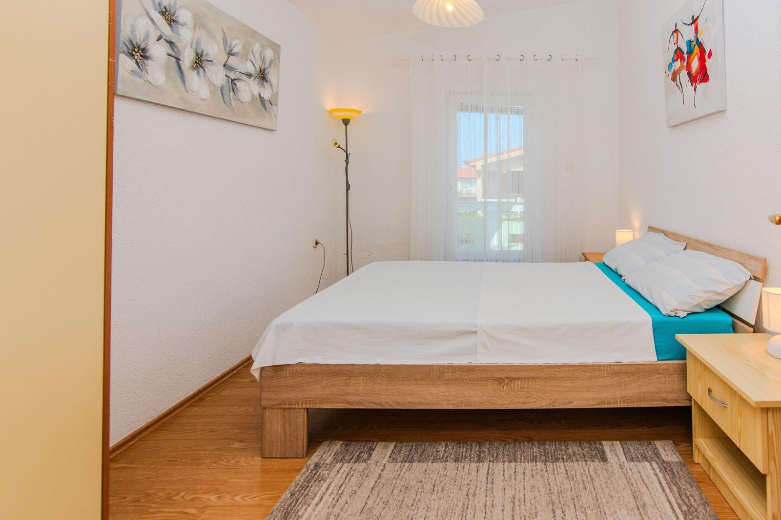 A bedroom with wooden bed, white walls, and window with curtains.