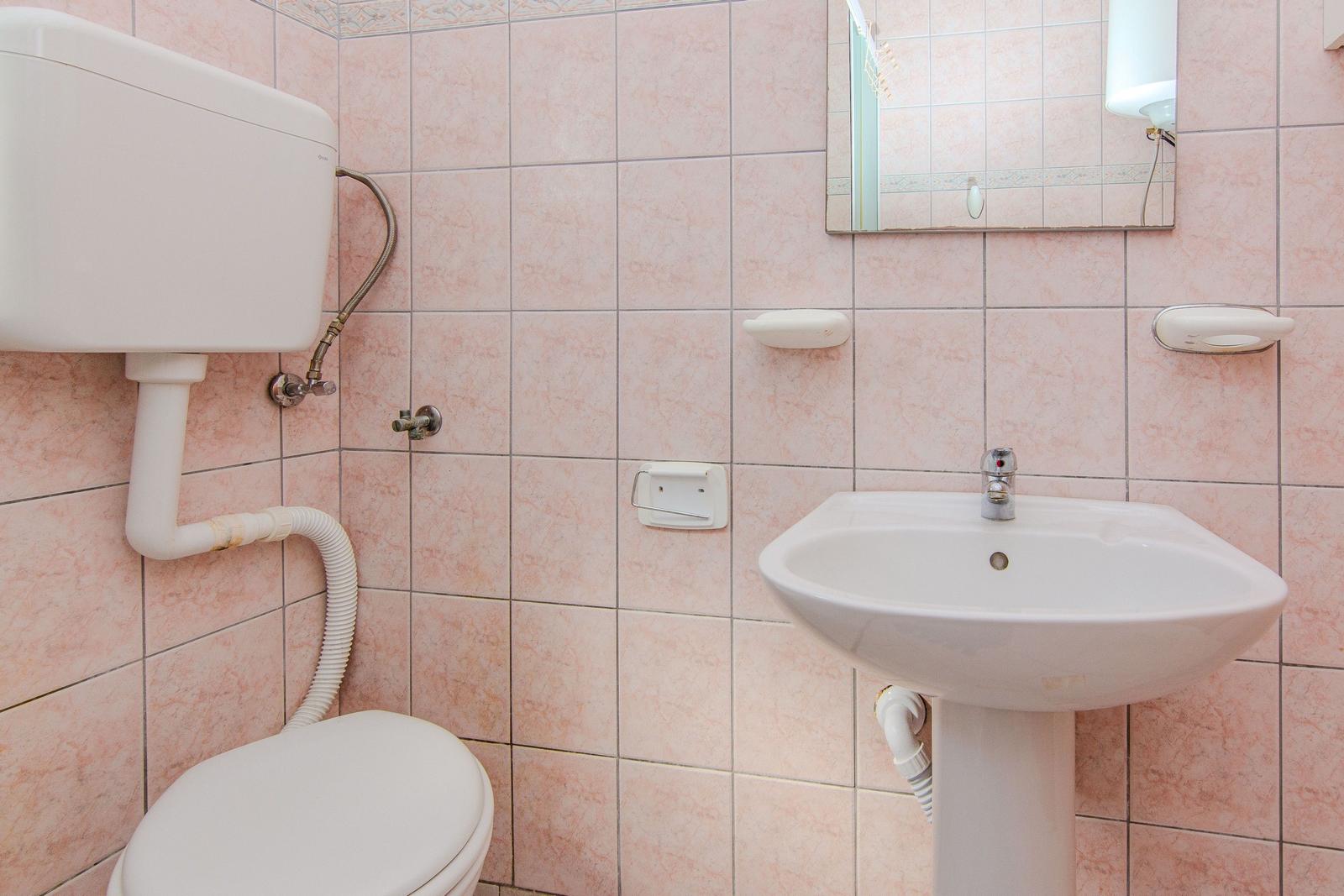 Bathroom with toilet, sink, and mirror on pink tiles.