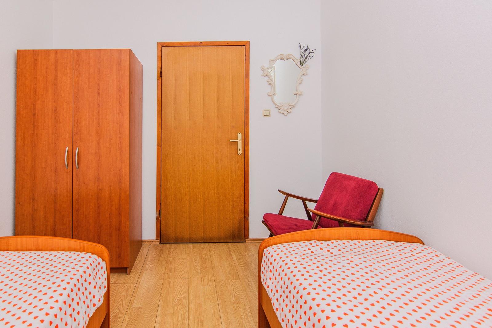 Two beds with orange pattern, wardrobe, door, and red seating.