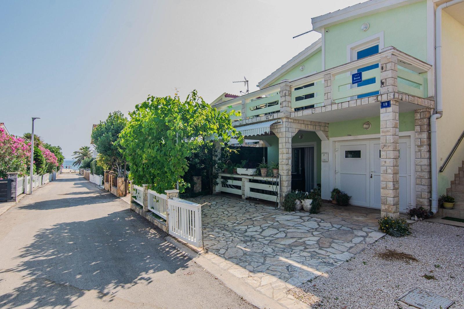 Green house with stone entrance and balcony, paved yard, sea view.