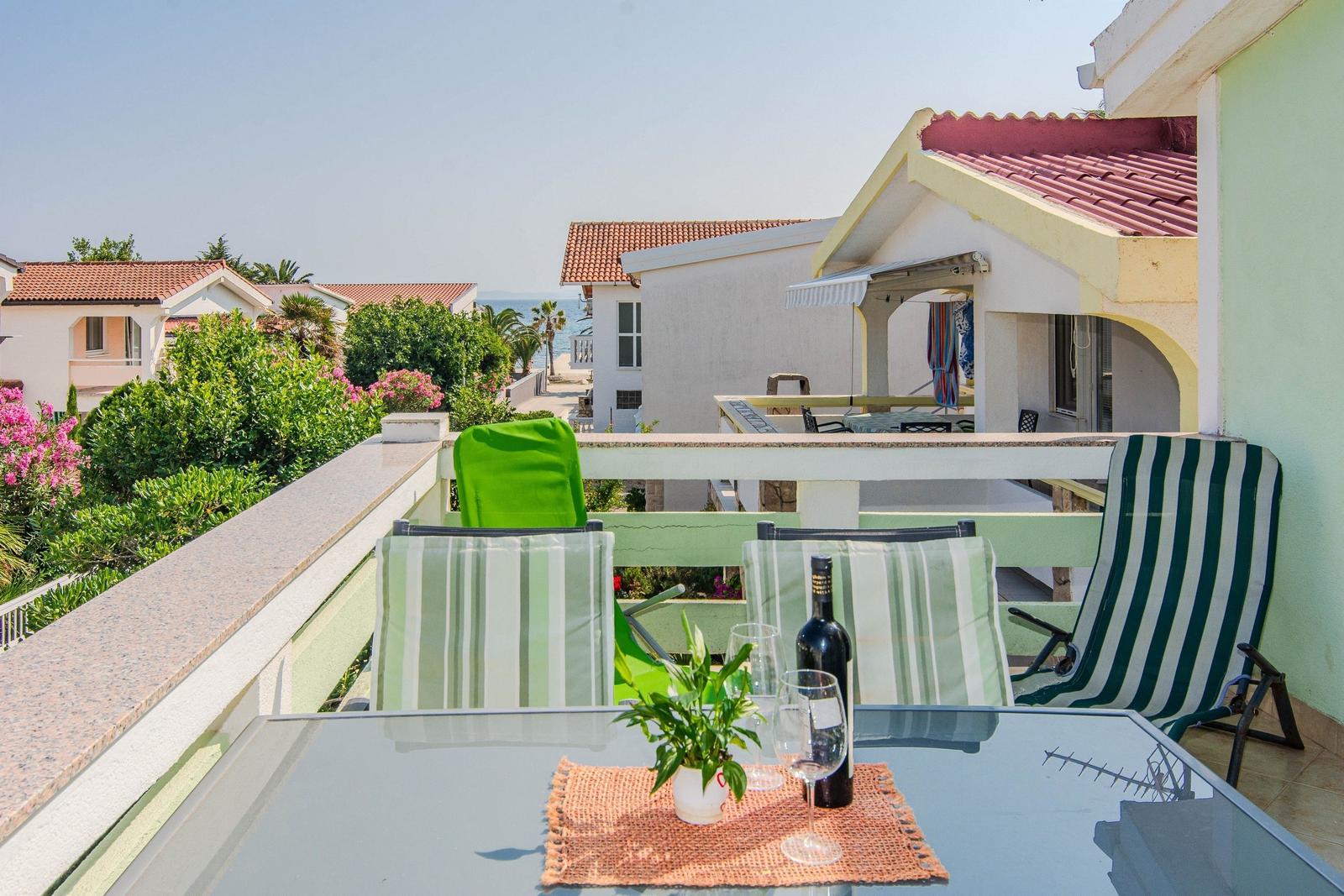 Terrace with table, chairs, and sea view. Wine bottle and plant on table.