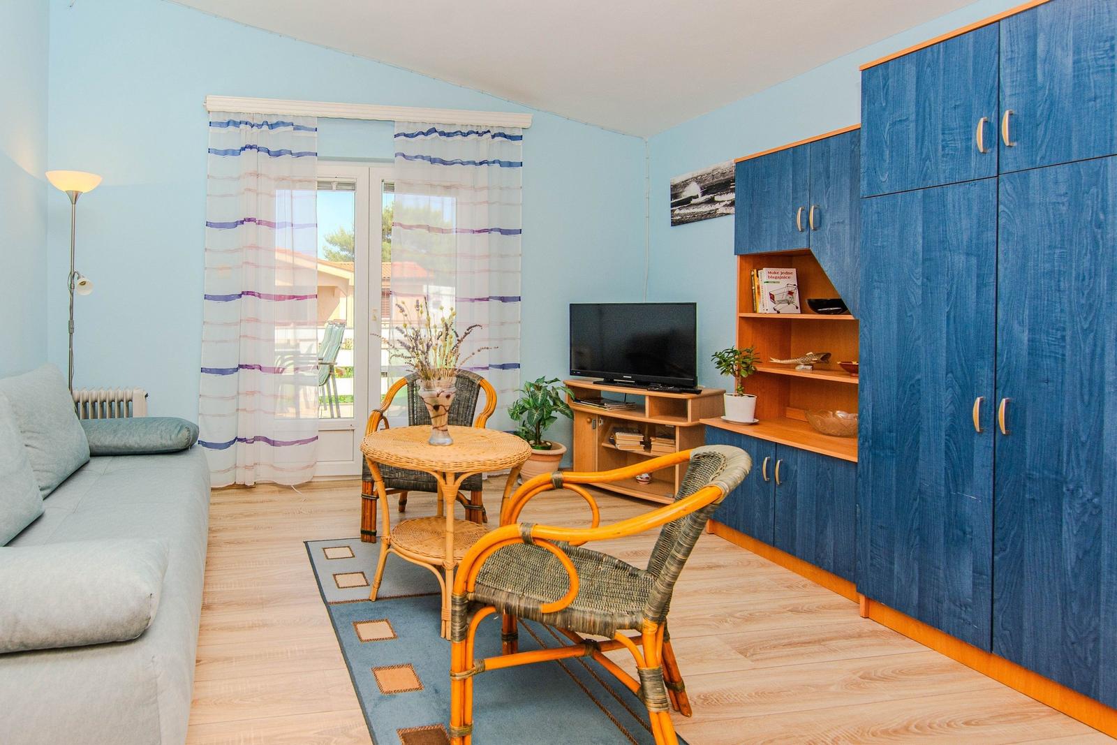 Living room with sofa, table, chairs, and TV. Blue cabinets and windows with curtains.