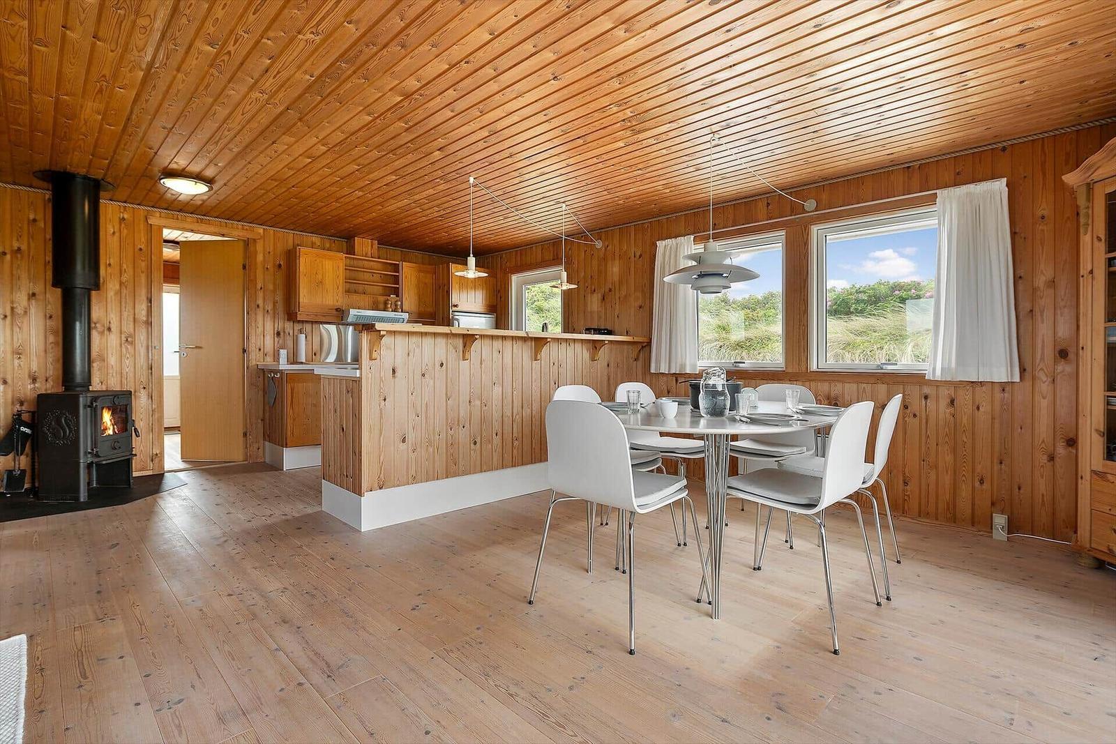 Holzgetäfelte Küche mit Esstisch und Kaminofen. Fenster zeigen Landschaft.