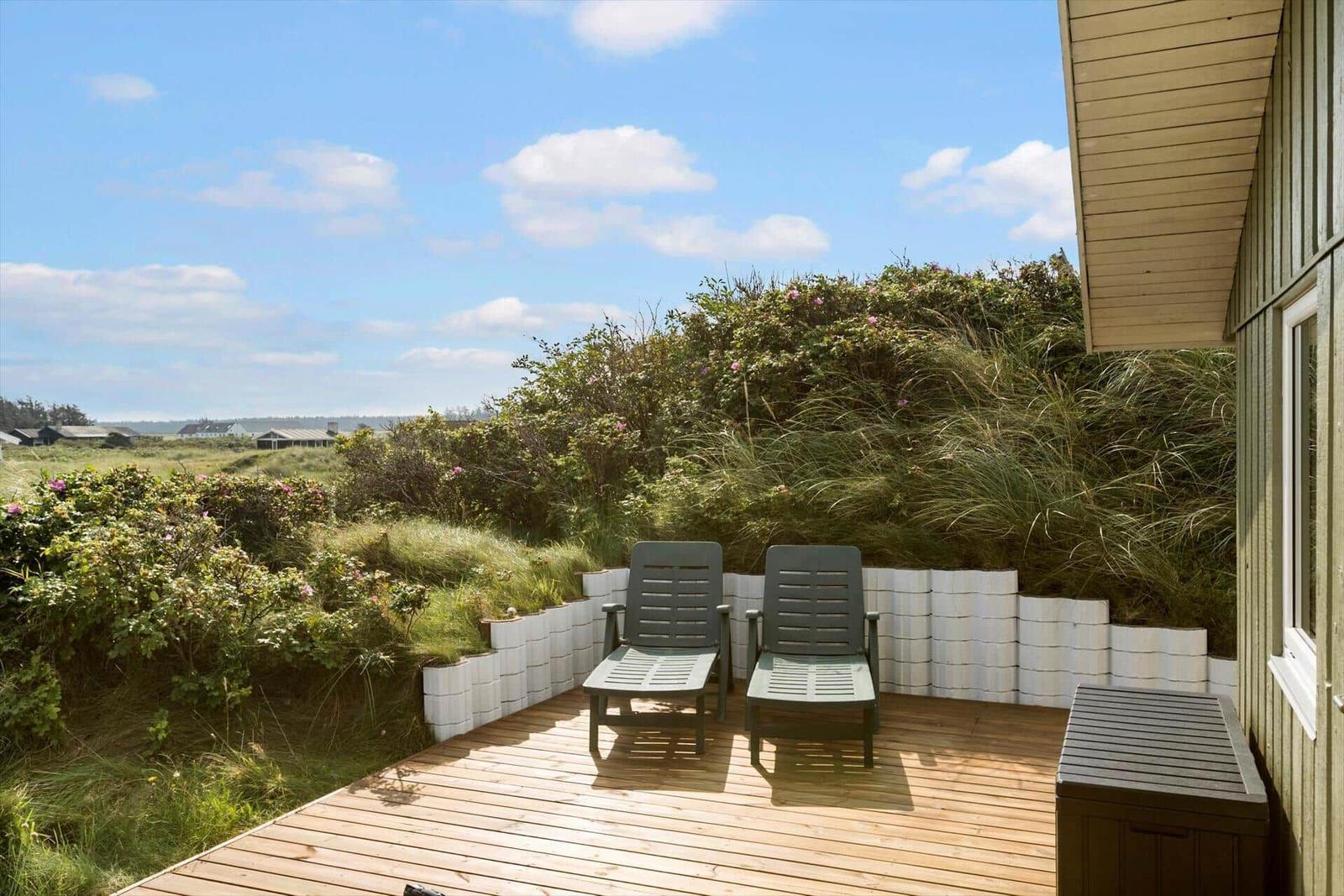 Terrasse mit zwei Liegestühlen und Blick auf grüne Dünen.