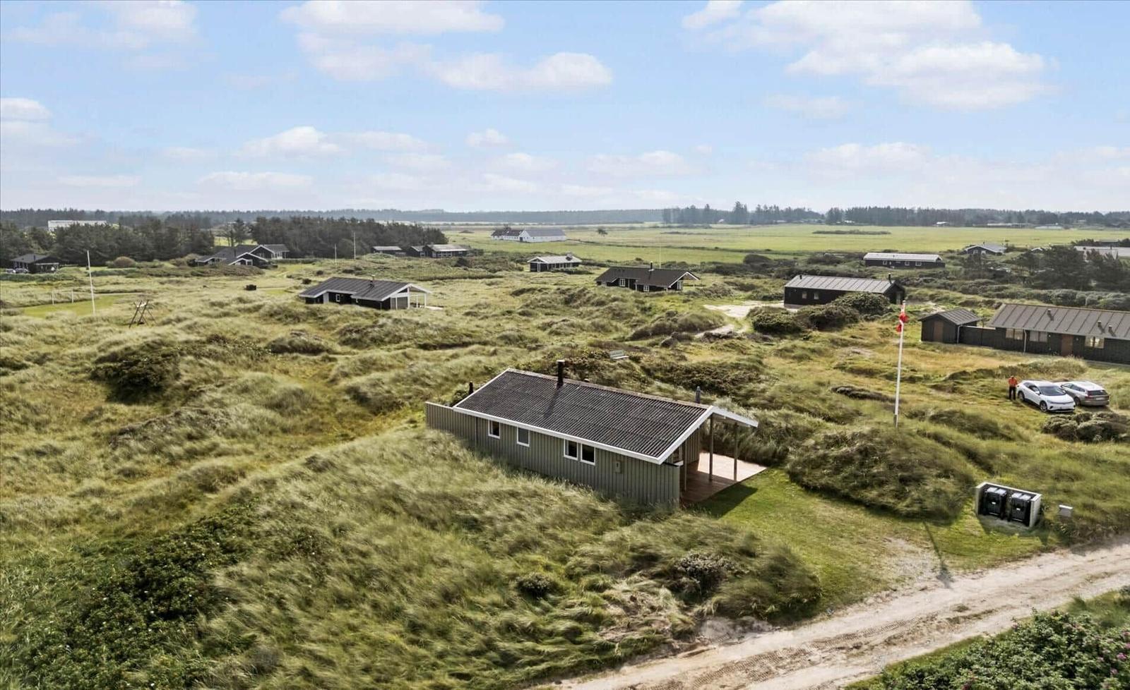 Haus auf grüner Dünenlandschaft mit mehreren Ferienhäusern im Hintergrund.