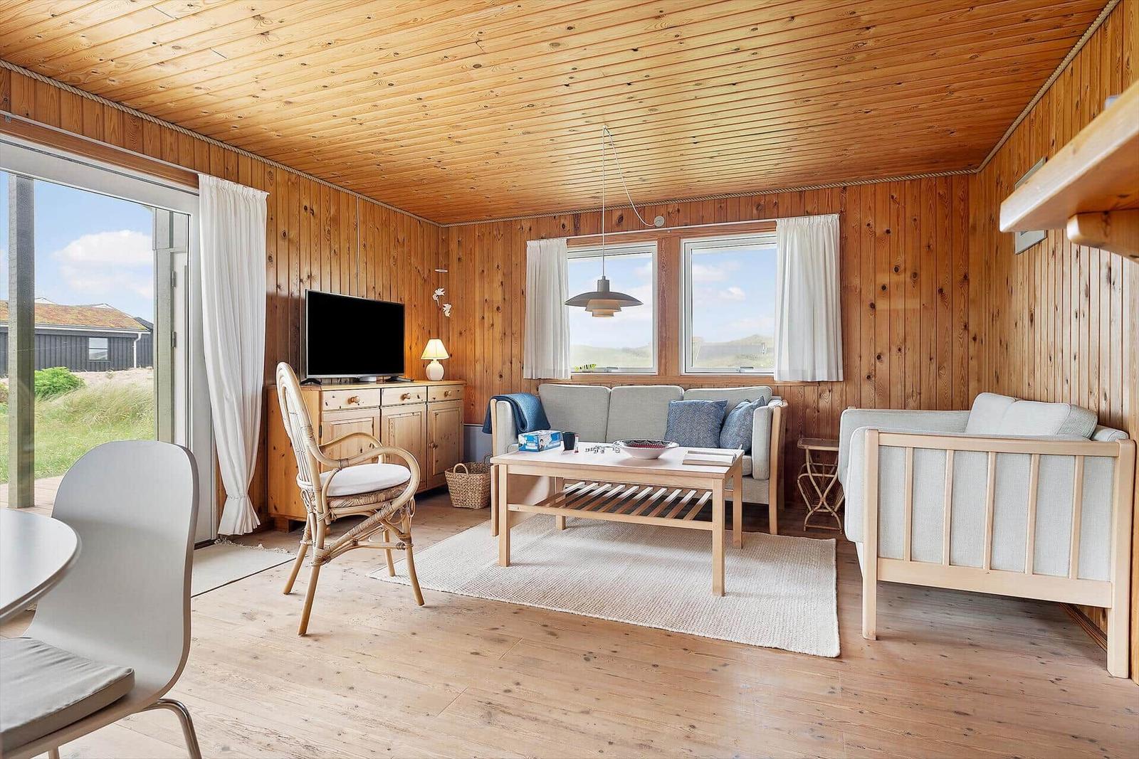 Wohnzimmer mit Holzwand, Sofa, Tisch und TV. Blick auf Außengelände.