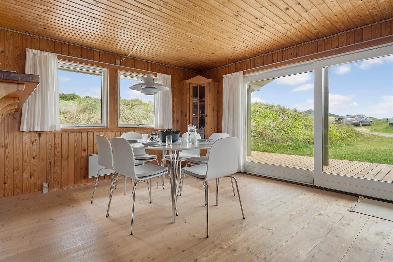 Esszimmer mit Holzdecke, Tisch und Stühlen. Blick auf Grasland durch Fenster und Glastüren.