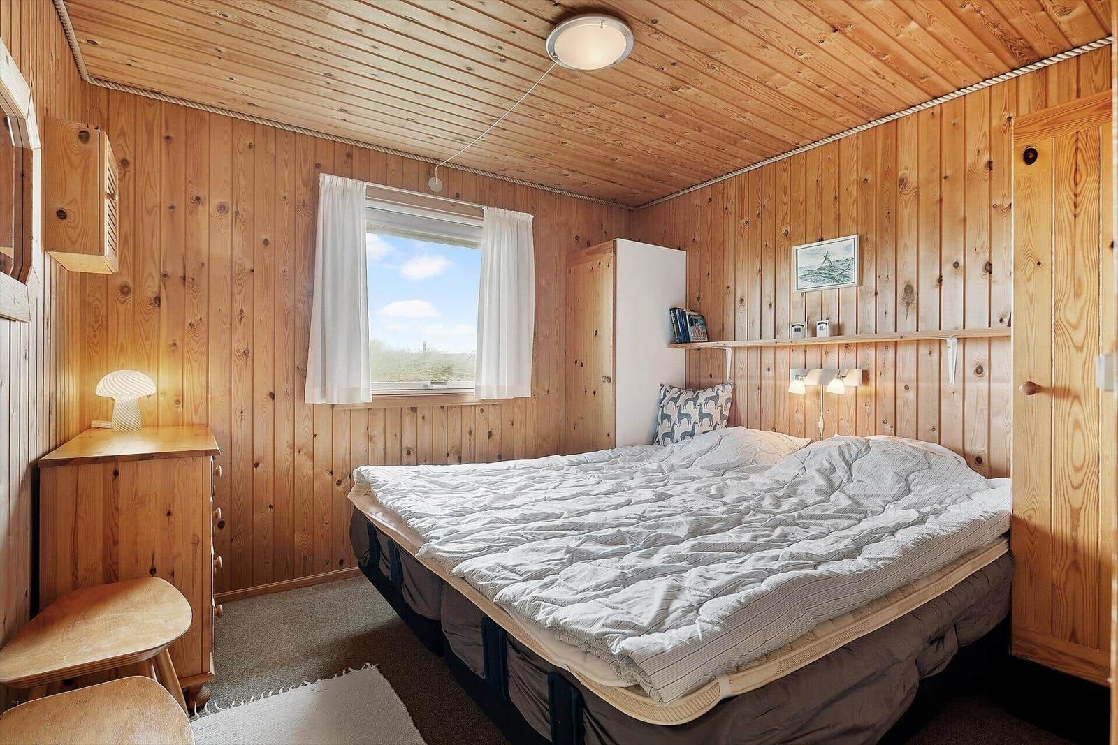 Schlafzimmer mit Holzwand, Bett, Fenster und Schrank.