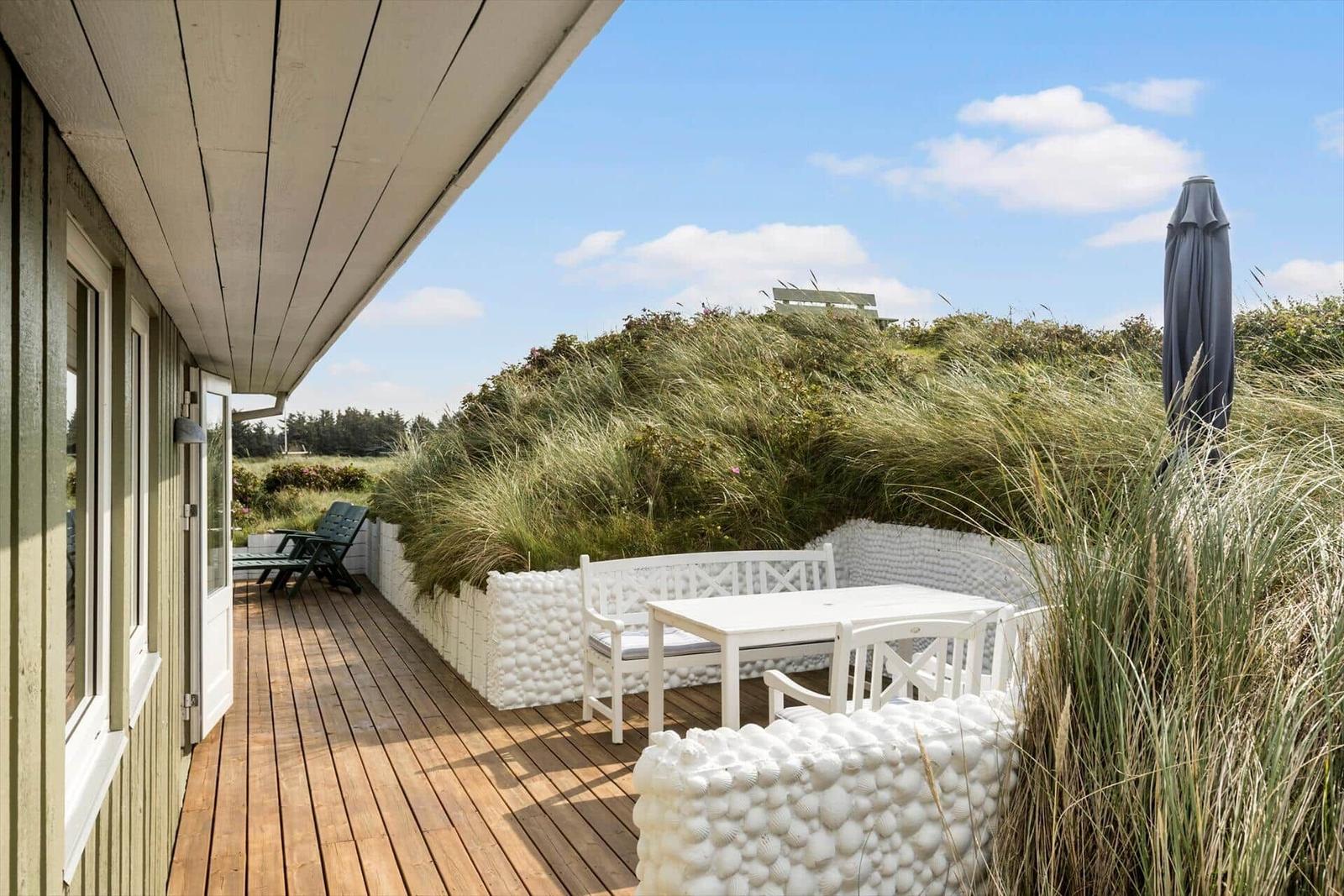 Terrasse mit weißem Tisch und Stühlen, umgeben von Schalenterrassen und Gras.