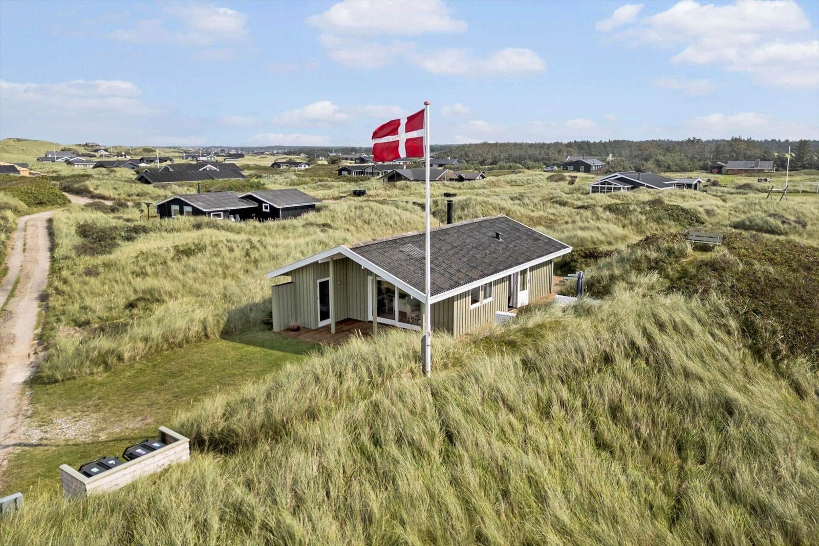 Haus mit dänischer Flagge auf Dünen, Blick auf Ferienhäuser im Hintergrund.
