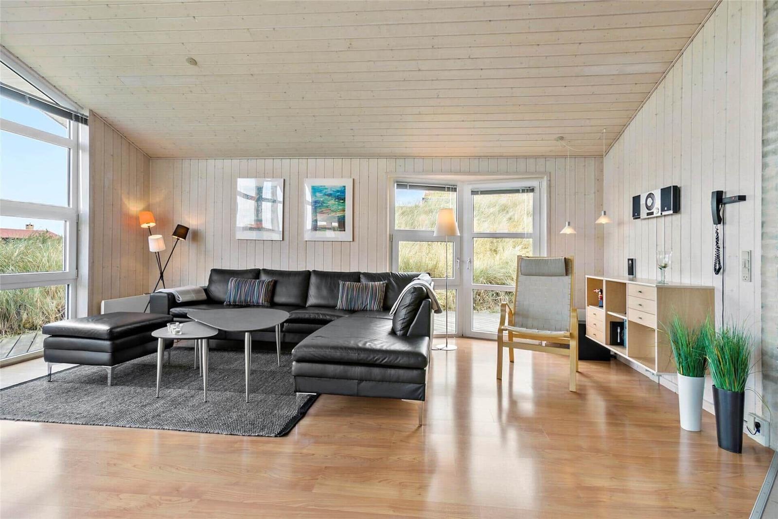 Wohnzimmer mit Ledersofa, Holzboden und großen Fenstern.