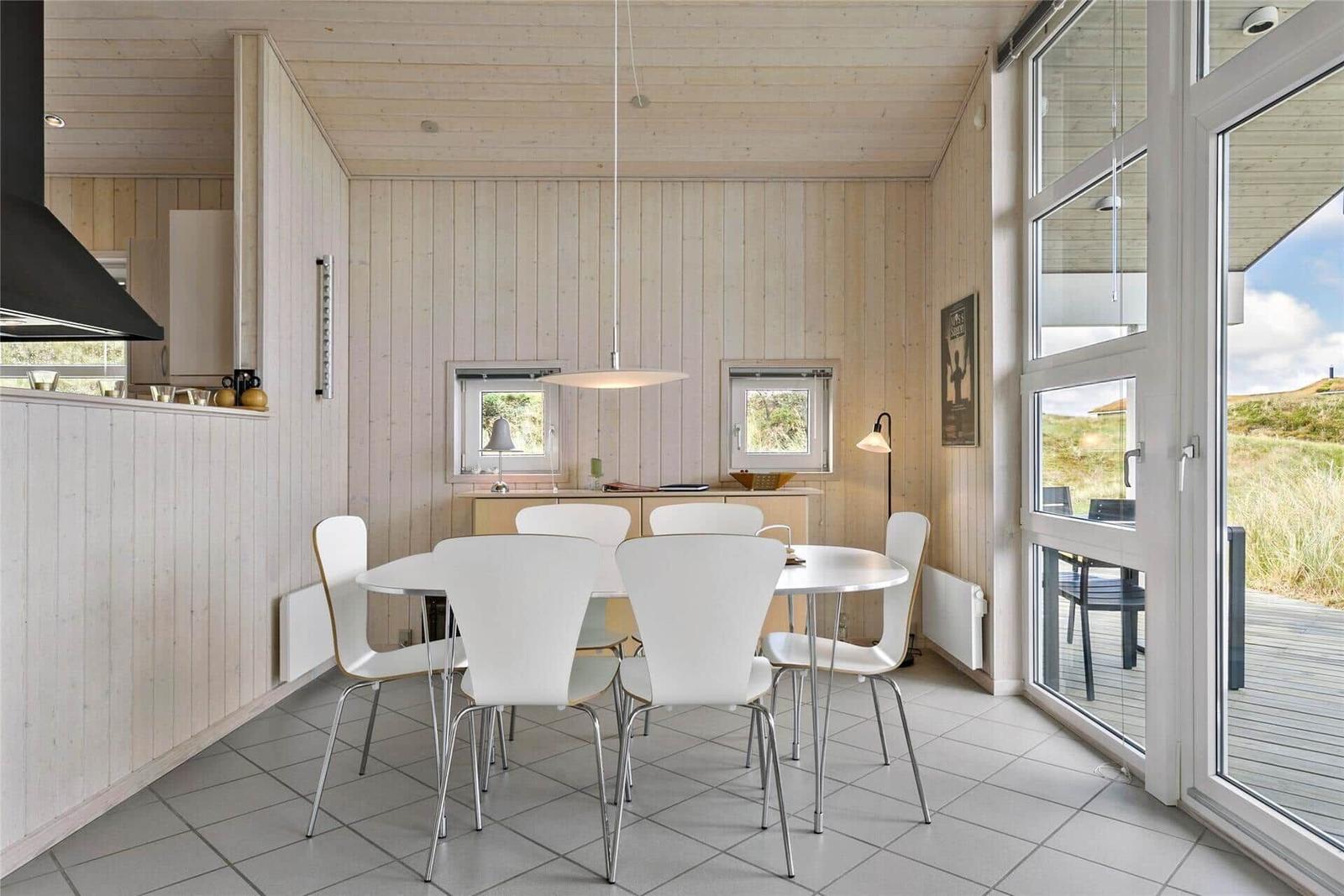 Essbereich mit weißem Tisch und Stühlen, Holzwände und großes Fenster mit Blick auf die Außenterrasse.