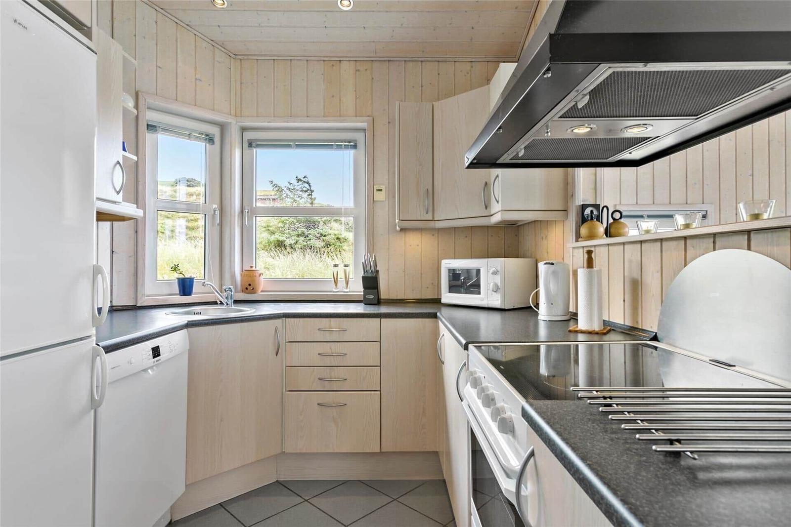 Küche mit Holzwand, Fenster, Küchenspüle und weißen Geräten.
