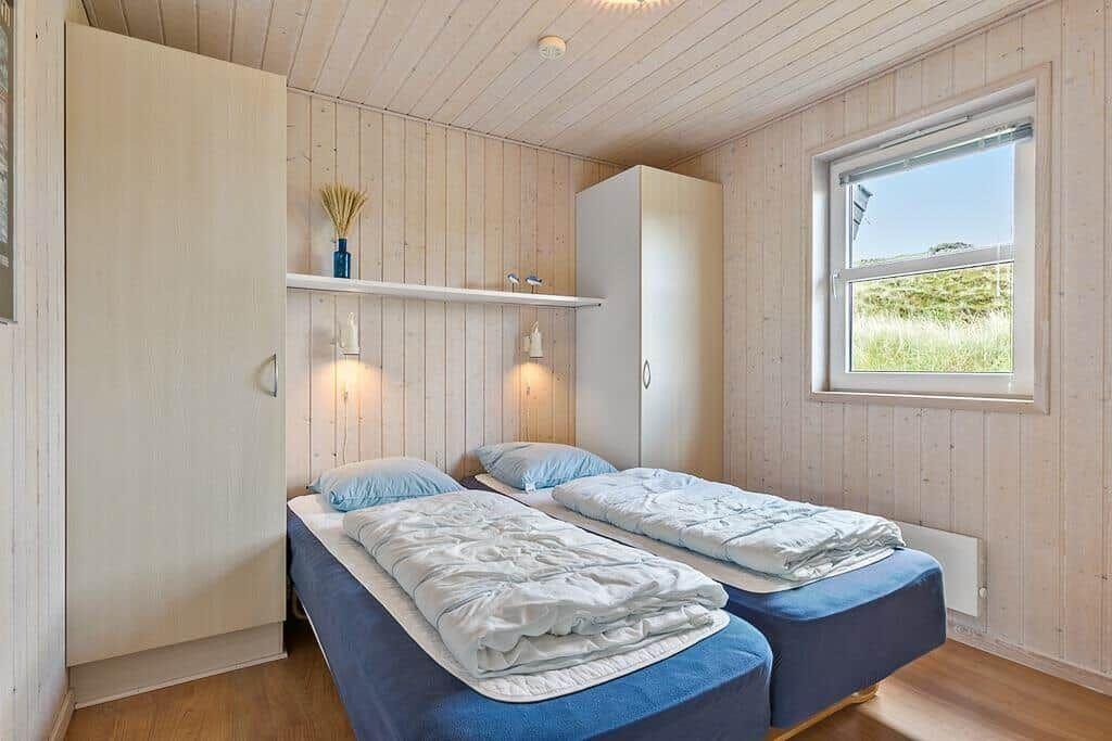 Zwei Betten mit blauen Matratzen und weißen Bettwäschen. Holzwände und ein Fenster mit Blick auf Gras.