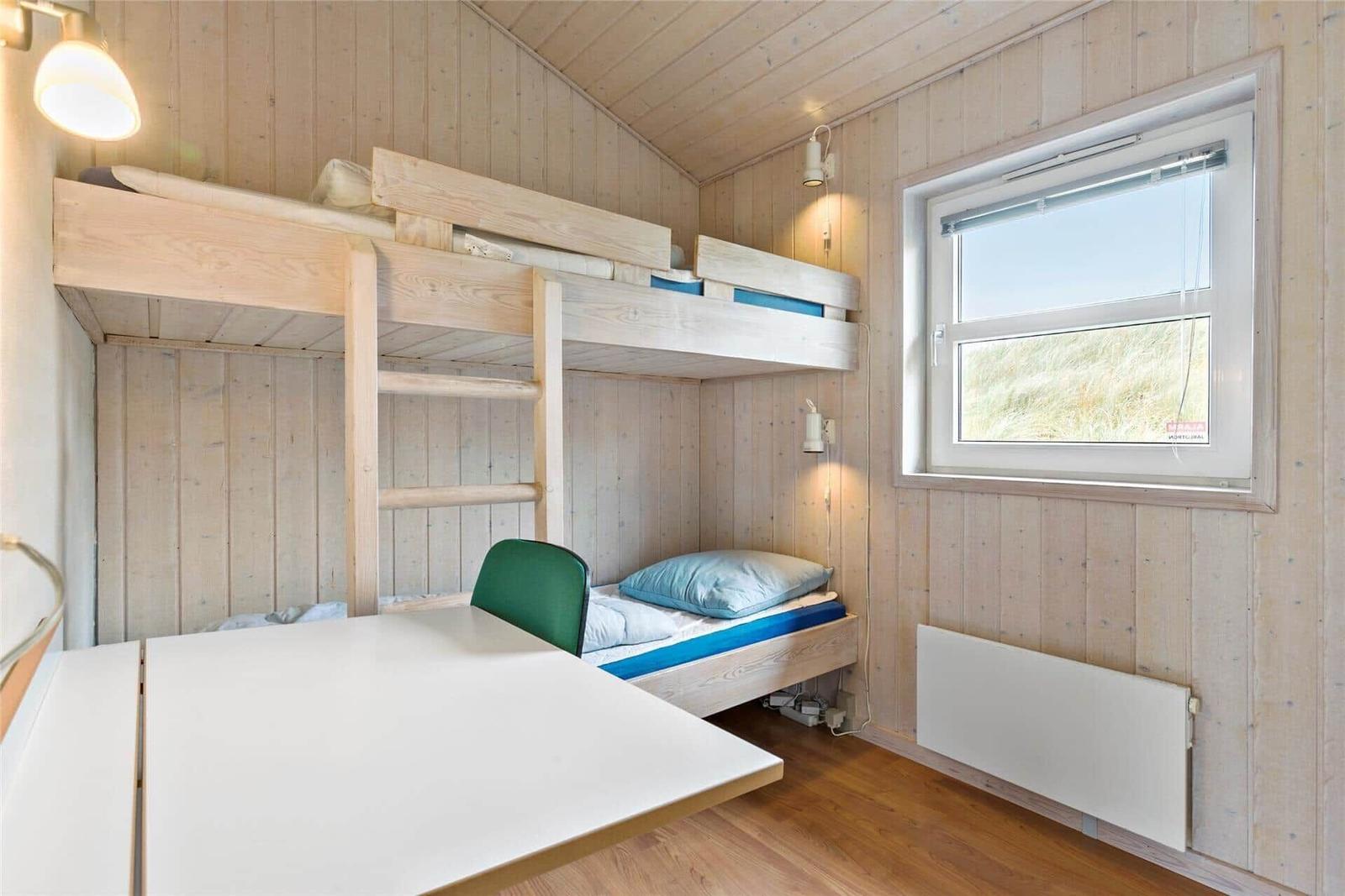 Zimmer mit Doppelstockbett, Tisch und grüner Stuhl. Holzwände und Fenster mit Blick.