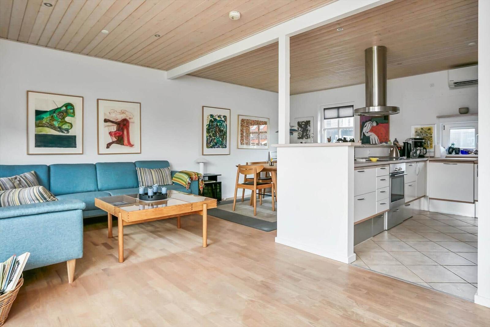 Wohn- und Küchenbereich mit Holzboden, blauem Sofa und moderner Küche.