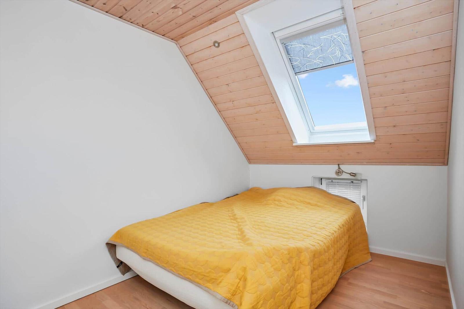 Schlafzimmer mit Dachschrägen, gelbem Bett und Dachfenster.