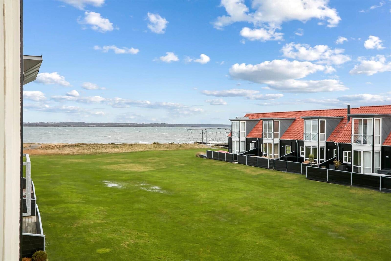 Grüner Rasenbereich mit Blick auf das Wasser und moderne Häuser mit roten Dächern.
