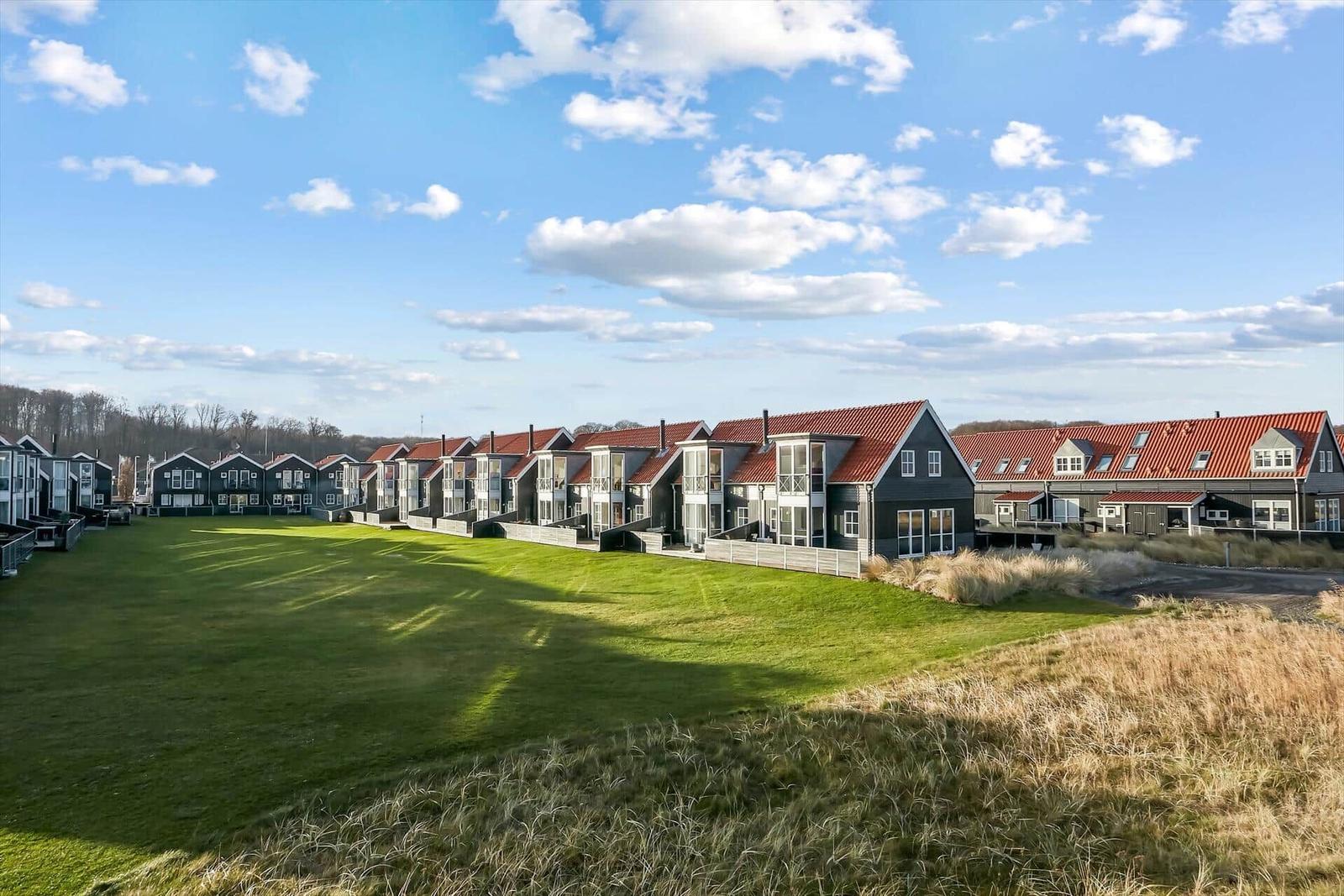 Reihen von Ferienhäusern mit roten Dächern und grünem Rasen vor blauem Himmel.