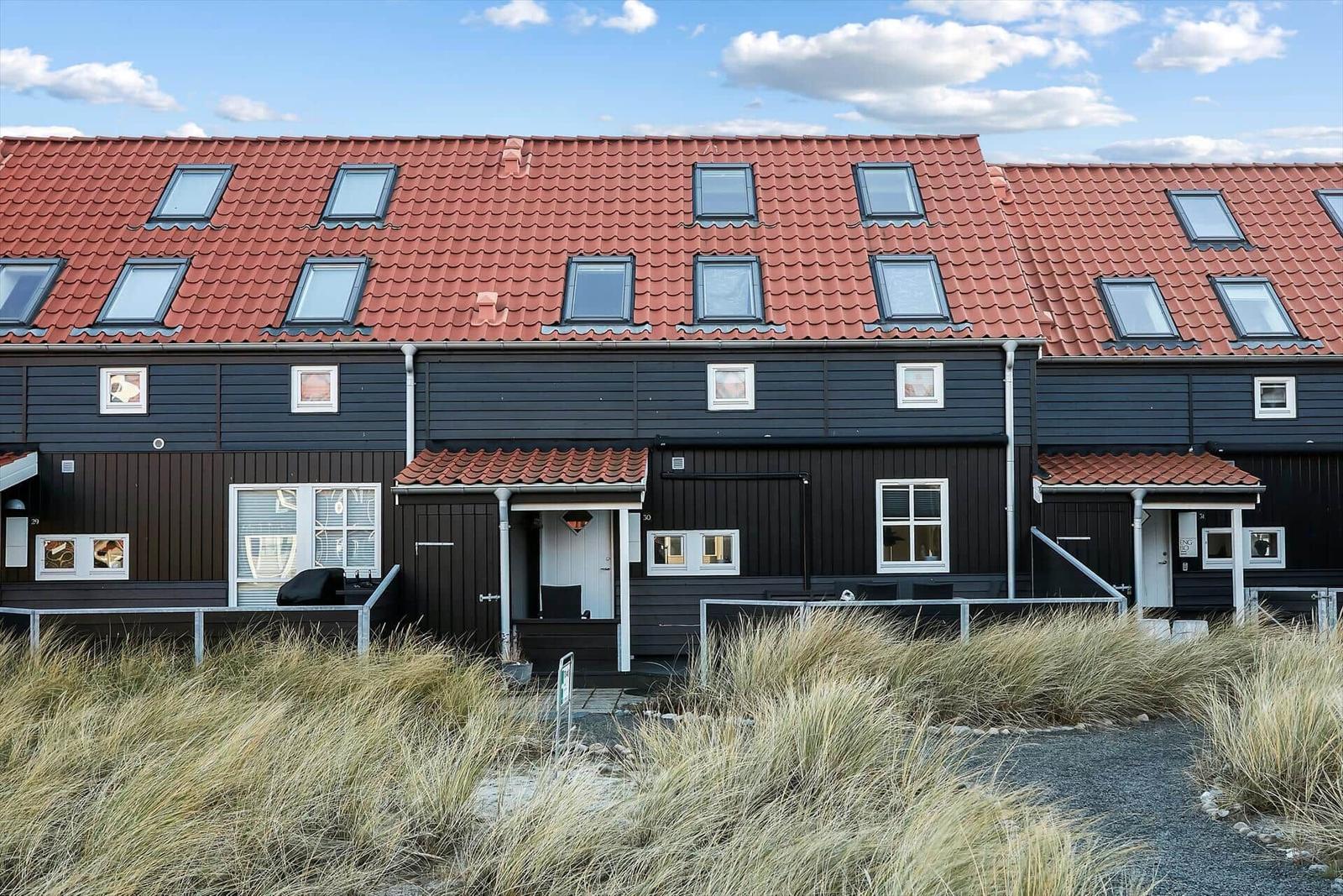 Schwarze Ferienhäuser mit rotem Dach und Dachfenstern. Vorhof mit Gras und Steinen.