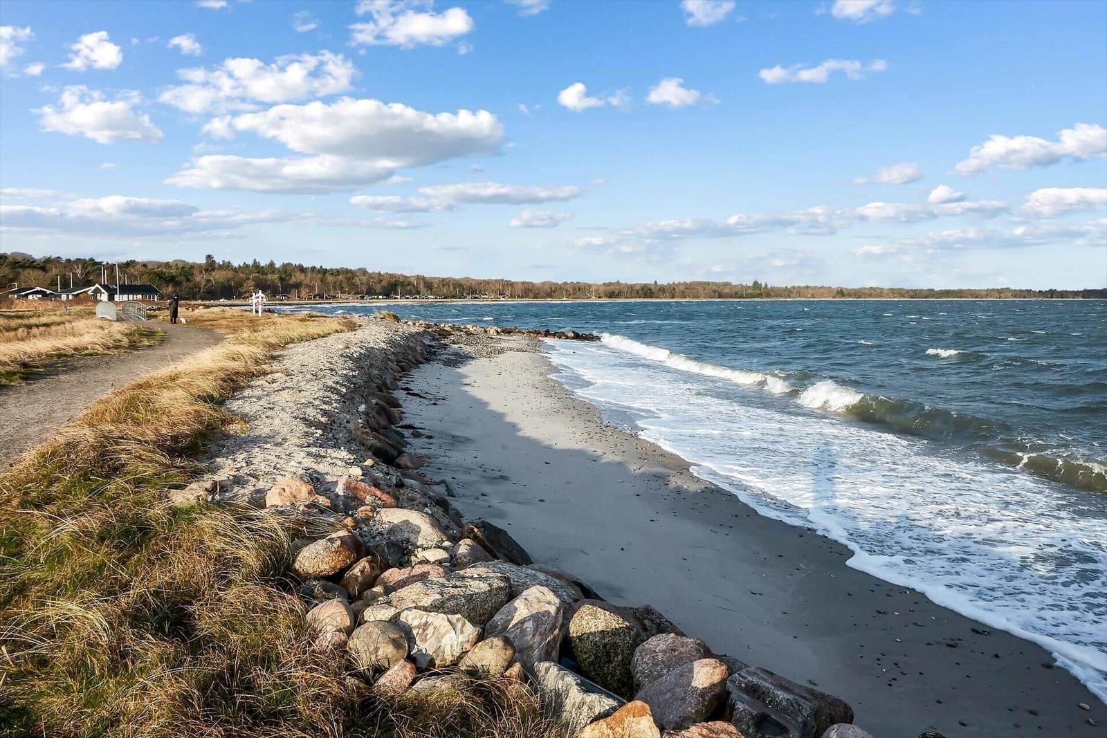 Strand mit Steinen und Wellen unter blauem Himmel mit Wolken.