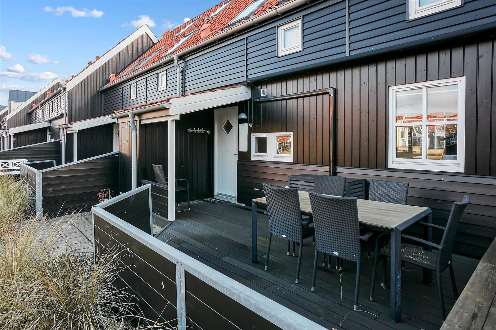 Terrasse mit Tisch und Stühlen vor einem Holzhaus mit weißen Fenstern.
