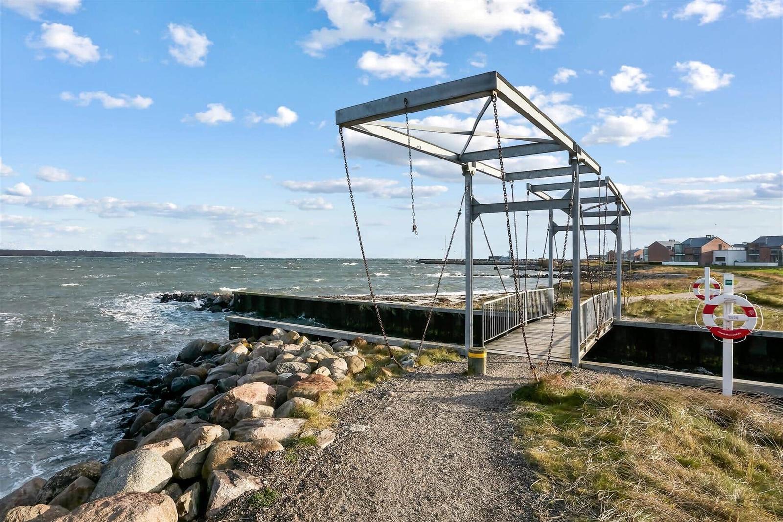 Metallbrücke mit Ketten über Steinhafen. Meer und Himmel im Hintergrund.