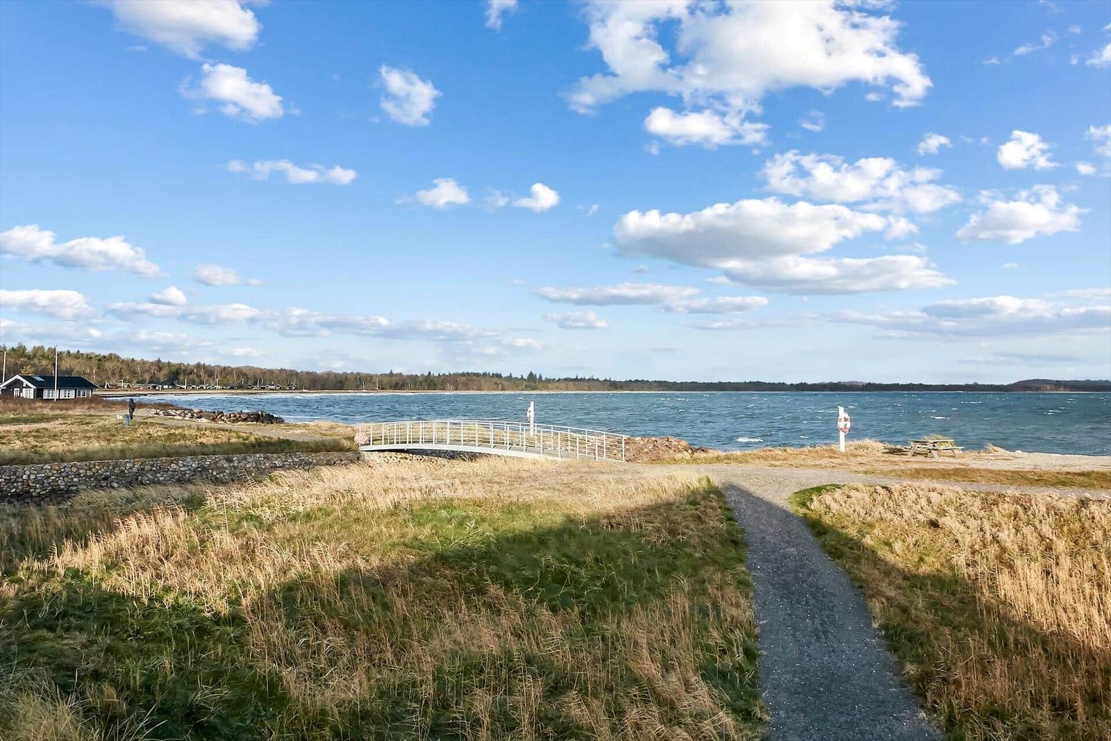 Weg führt über Brücke zum Strand mit Blick auf See und Wald.