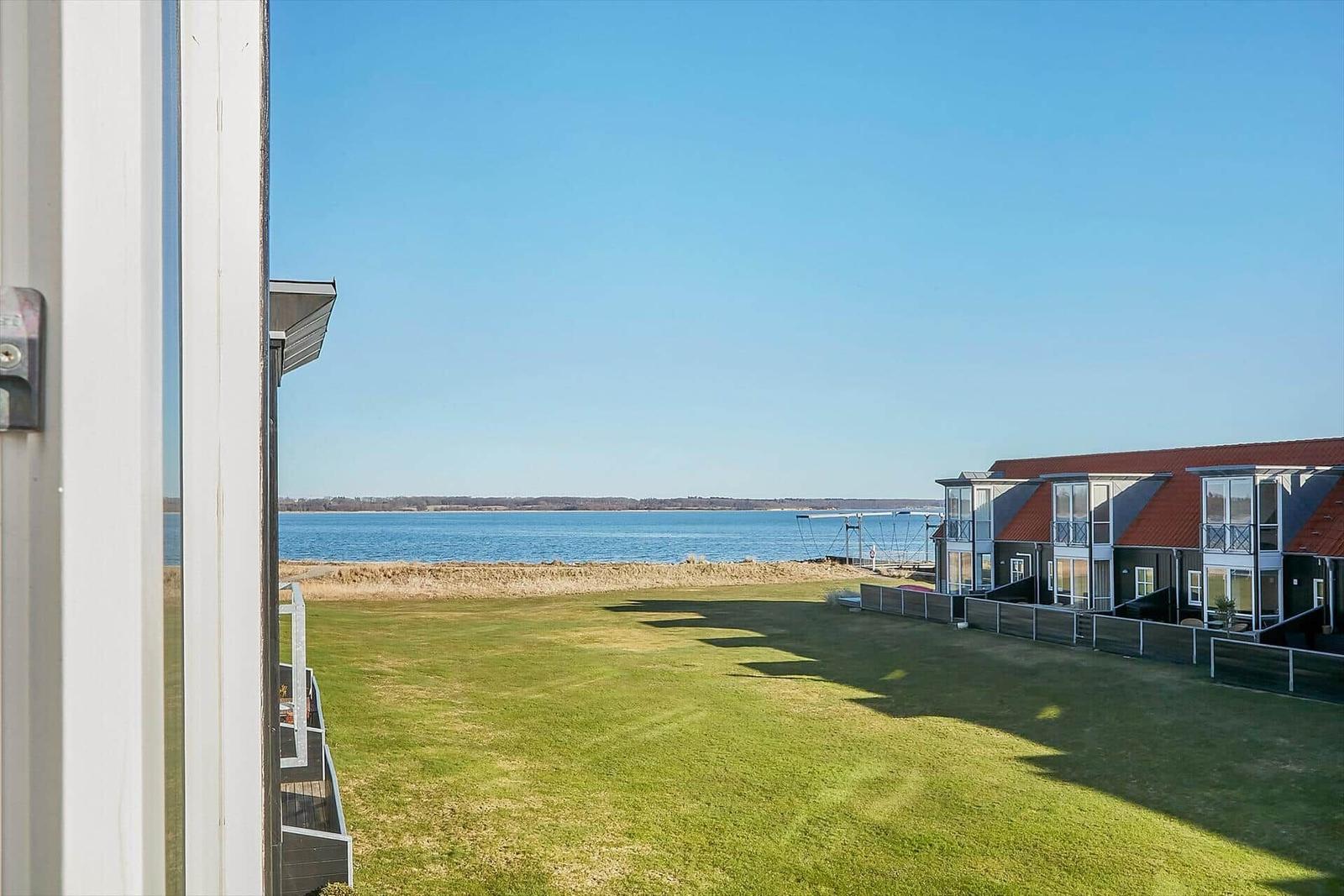Blick auf einen grünen Rasenbereich mit See und modernen Häusern im Hintergrund.