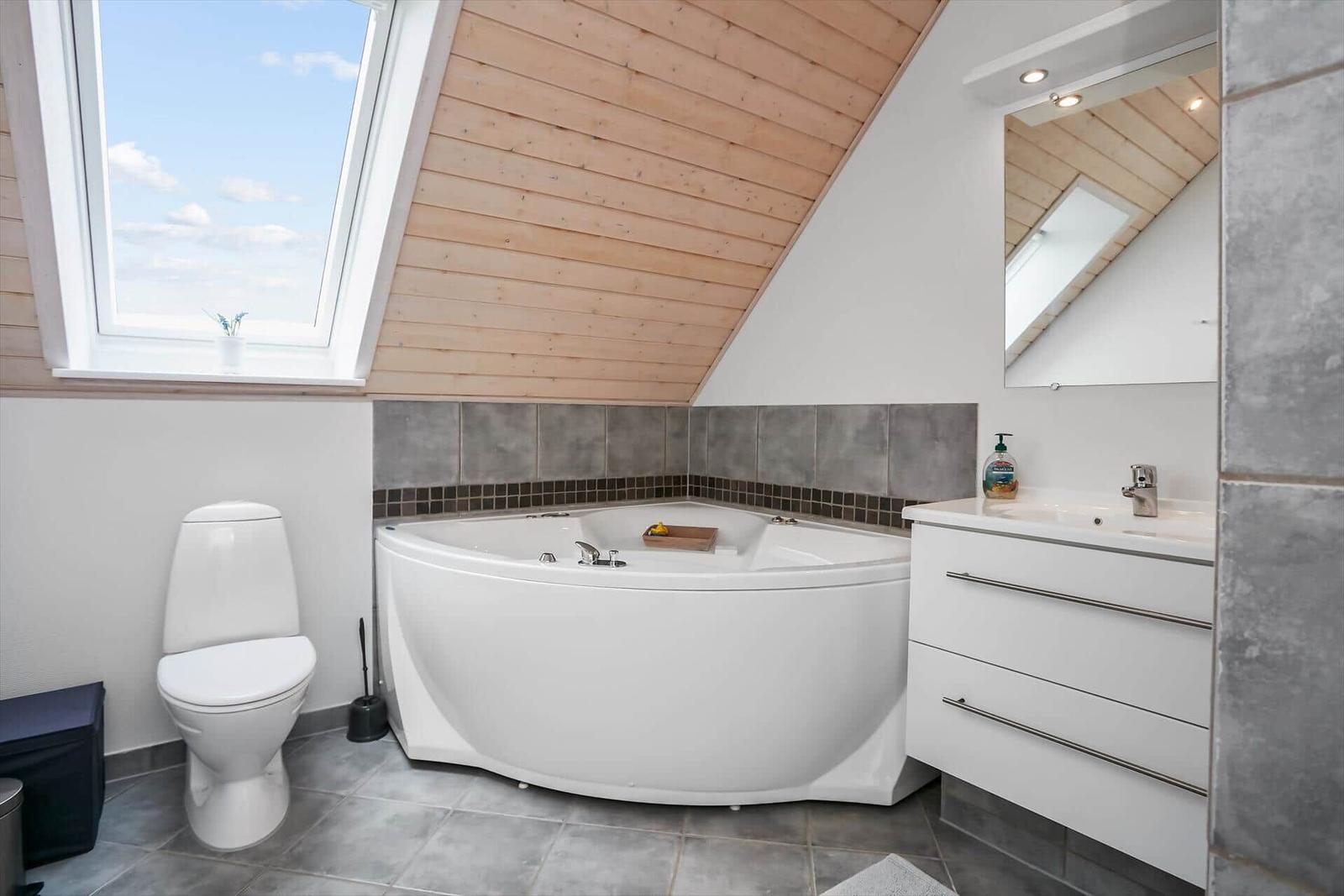 Badezimmer mit Dachfenster, Badewanne, Waschbecken und Toilette.