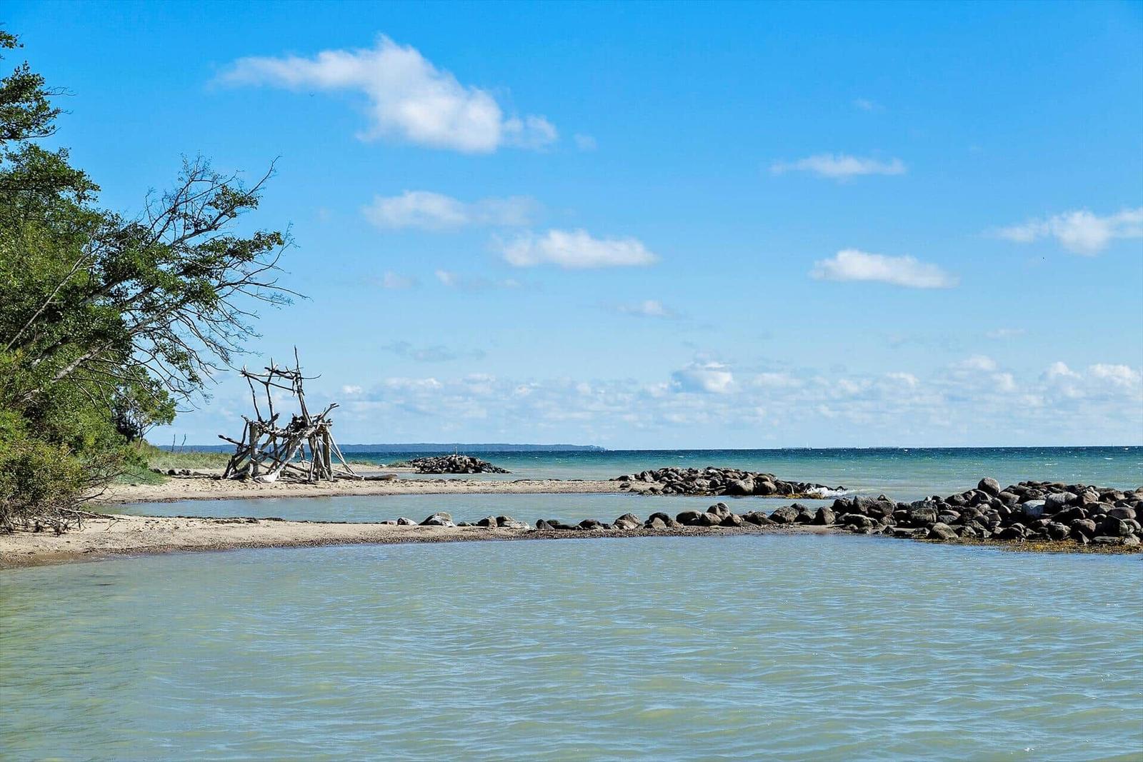 Strand mit Steinen und Holzkonstruktion am Wasser.
