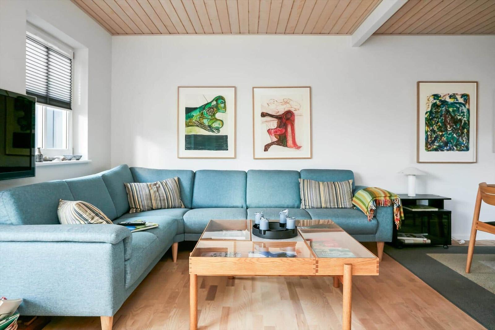 Ein Wohnzimmer mit blauem Sofa, Glas-Tisch und Wandbildern.