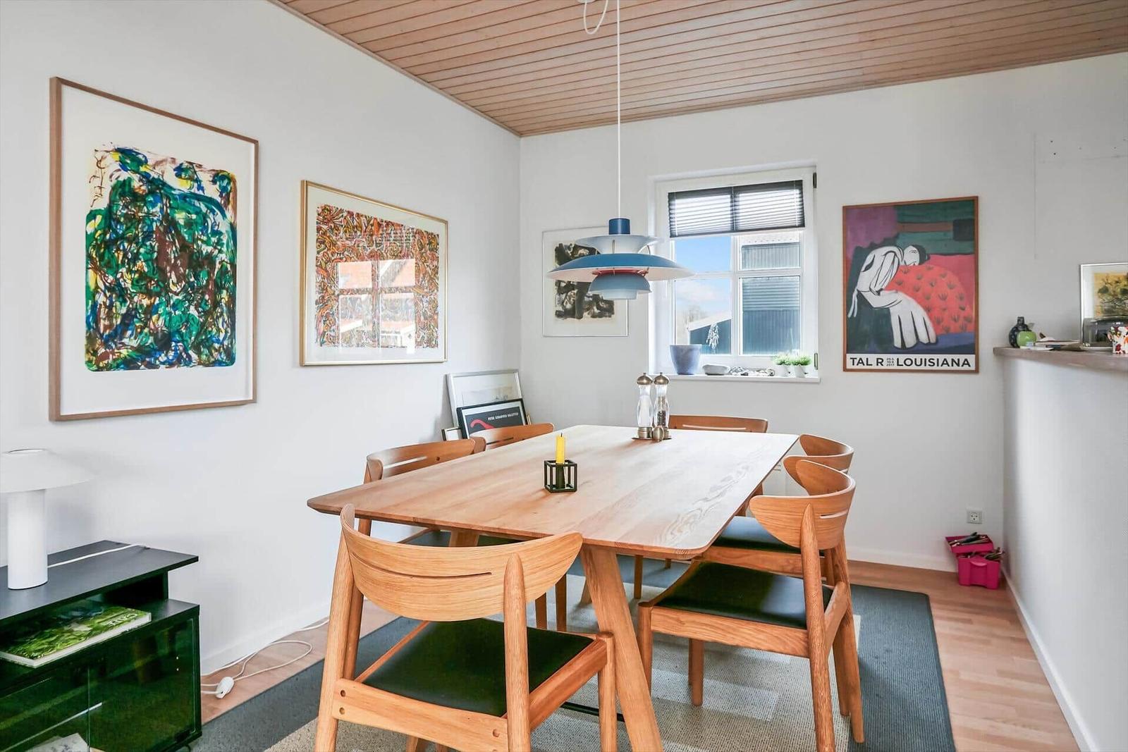 Esszimmer mit Holztisch, Stühlen und Wandbildern. Decke aus Holz.