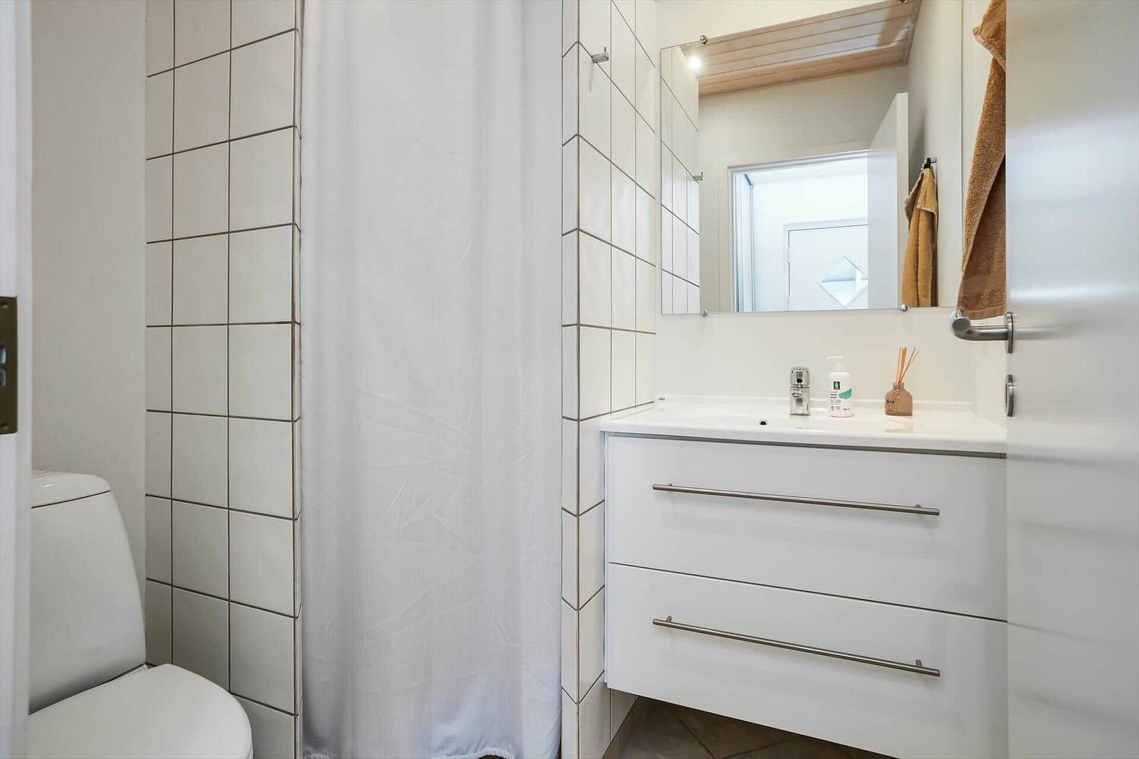 Badezimmer mit Toilette, Duschvorhang und Waschbecken mit Spiegel.