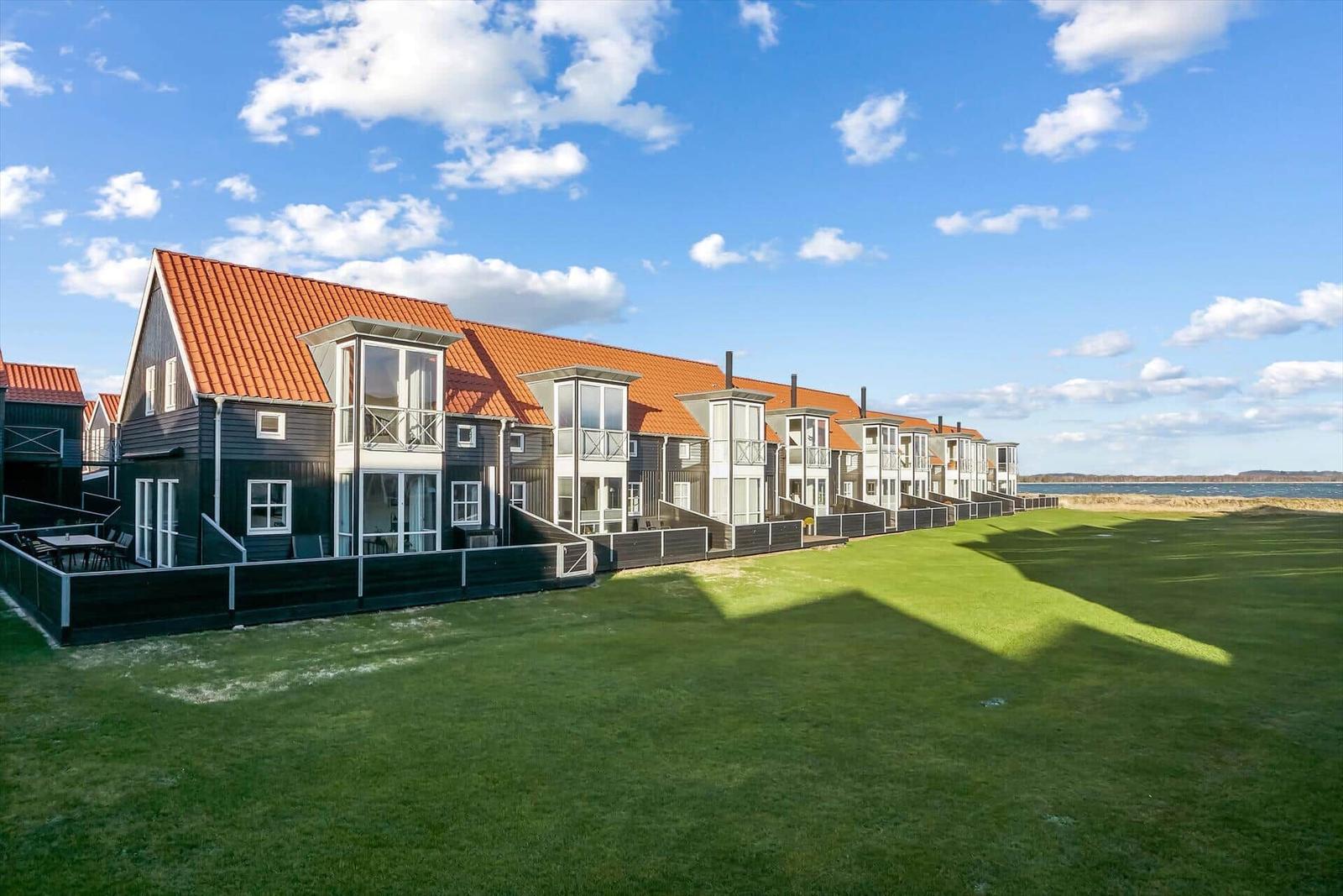 Reihenhaus mit rotem Dach und grünem Rasen vor Wasser.