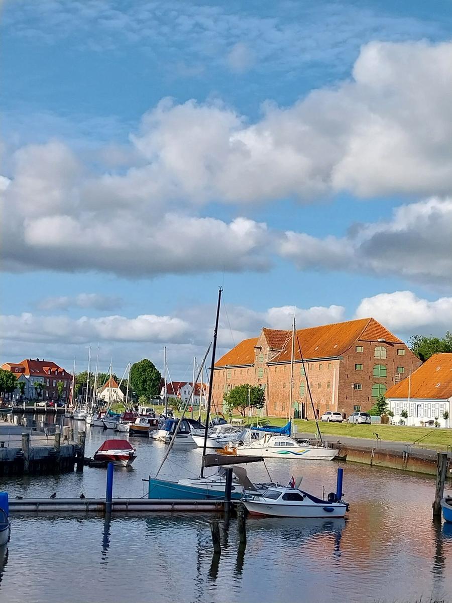 Hafen mit Booten und roten Dächern unter blauem Himmel mit Wolken.