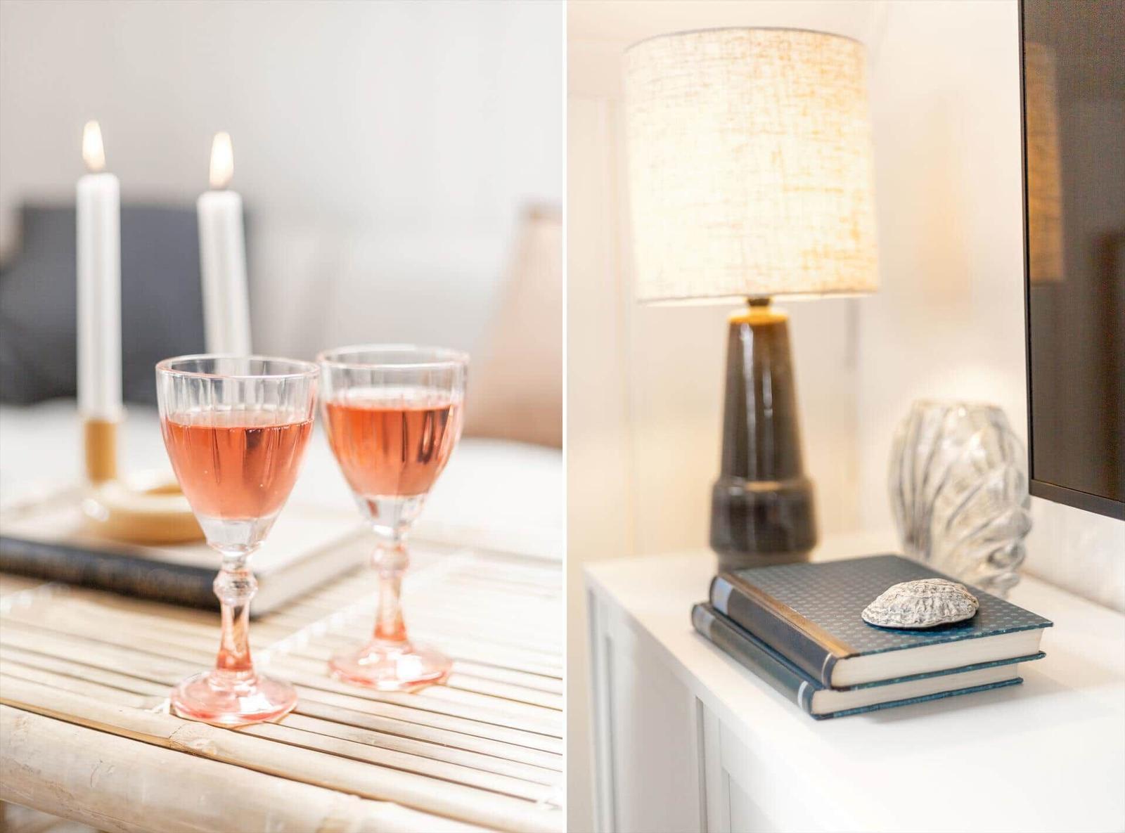 Zwei Gläser Rosé auf einem Tisch mit Kerzen. Lampe, Bücher und Muschel auf einem Nachttisch.