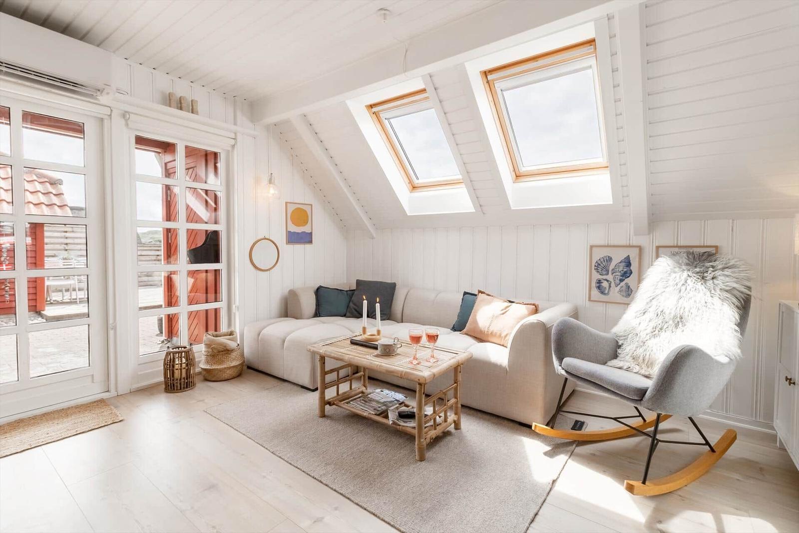 Wohnzimmer mit Sofa, Schaukelstuhl und Dachfenstern. Holzboden und weiße Wände.