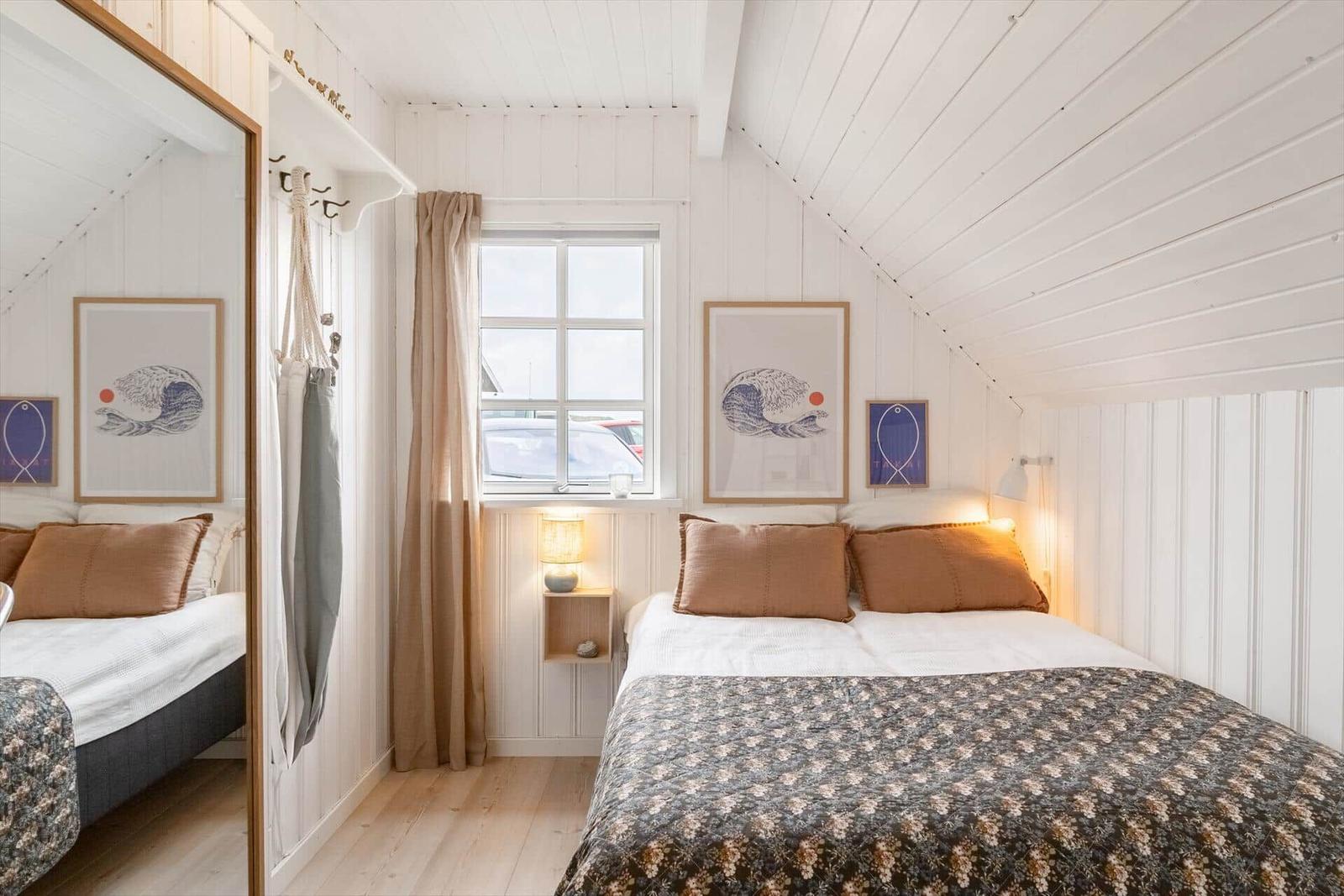 Schlafzimmer mit Bett, Fenster und Wandbildern.