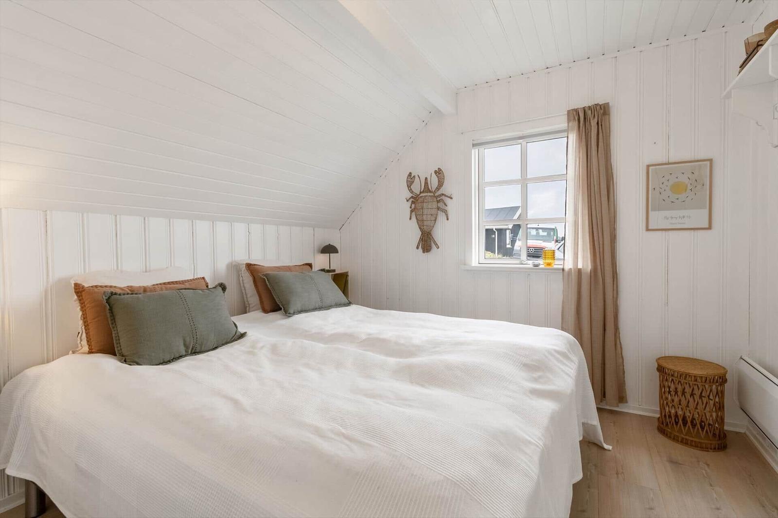 Schlafzimmer mit Dachschräge, weißem Bett und Fenster mit Vorhang.