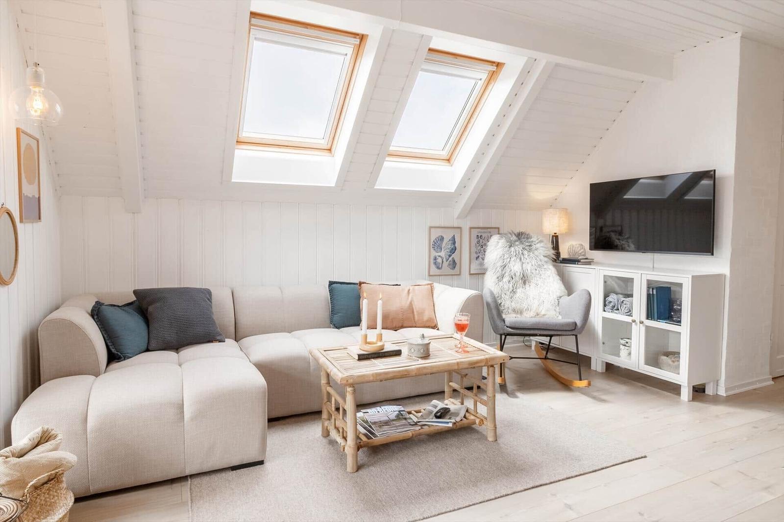 Wohnzimmer mit Sofa, Couchtisch und Fernseher unter Dachfenstern.