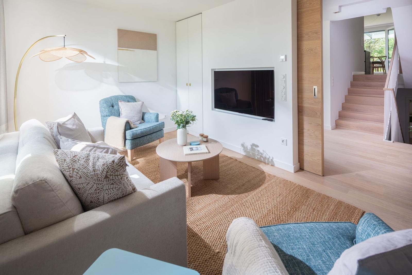 Wohnzimmer mit Sofa, Sessel, Couchtisch und Fernseher. Holzdielen und Teppichboden.