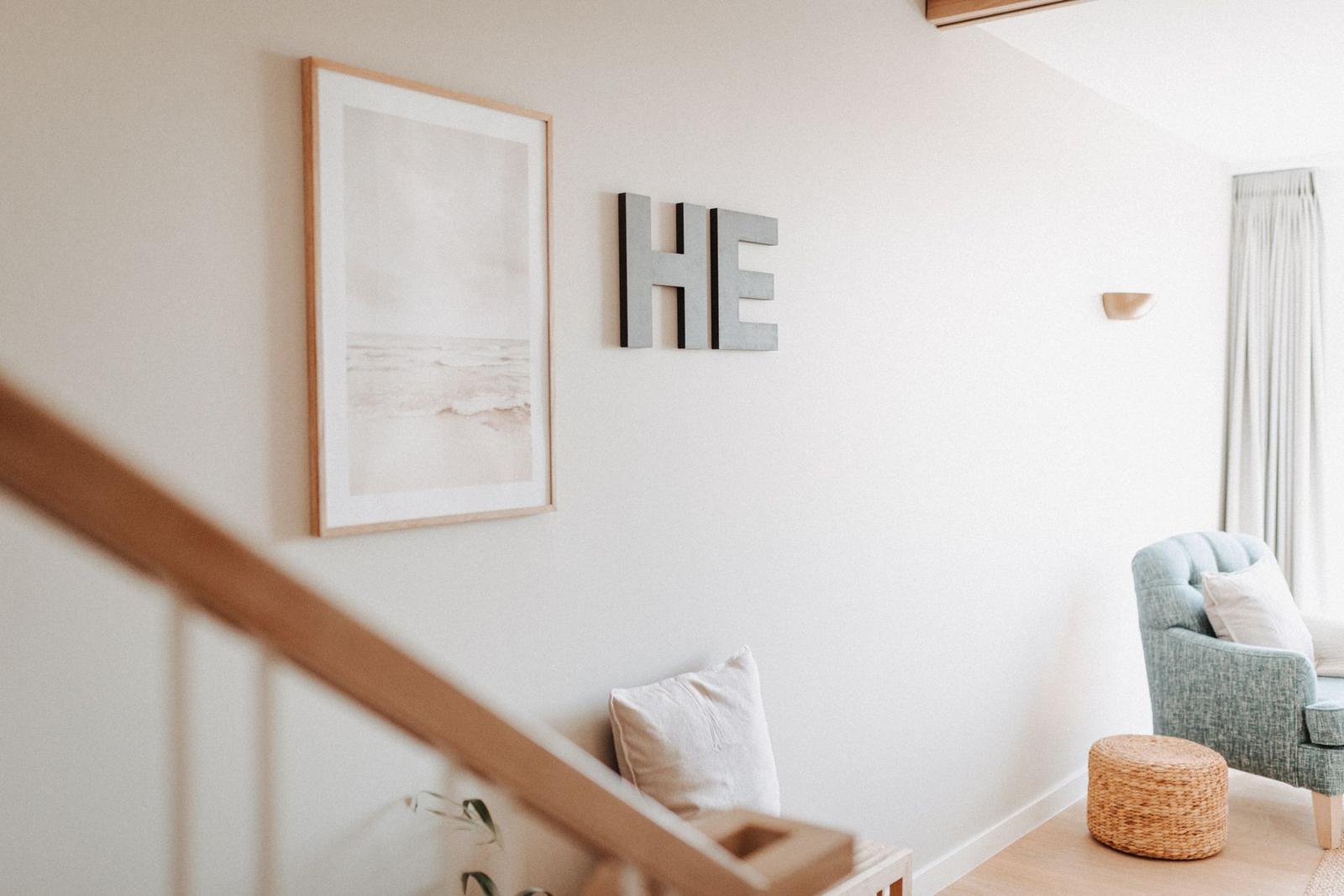 Wohnbereich mit Sessel, Wandbild und Buchstaben. Treppenhaus im Vordergrund.