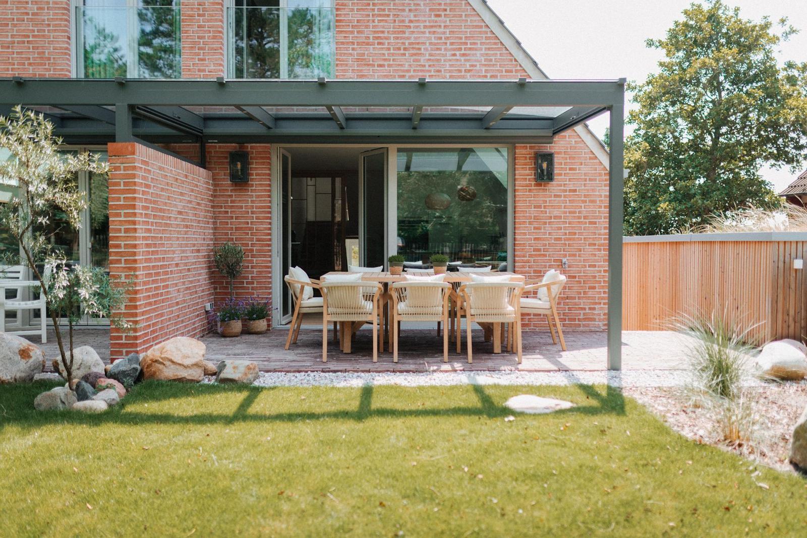 Terrasse mit Sitzgruppe unter Dach, umgeben von Gras und Steinen.