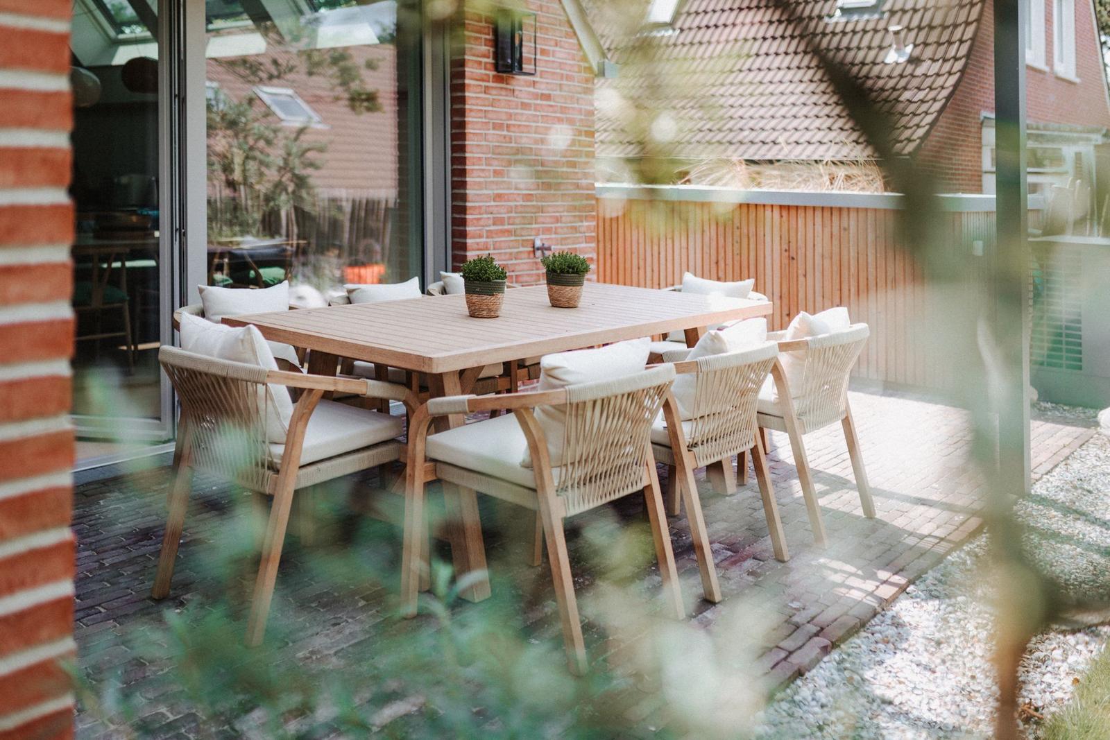 Terrasse mit Holztisch und Stühlen, Pflanzen und Blick auf Haus.