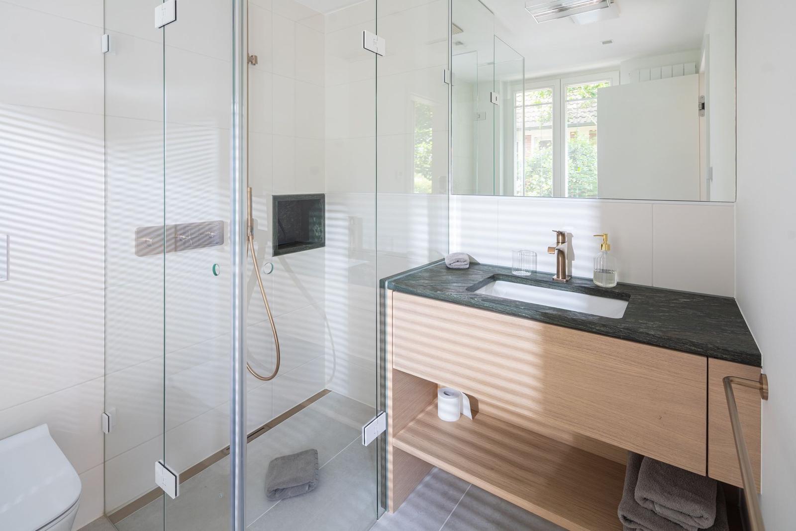 Bad mit Dusche, Waschbecken und Toilette. Moderne Einrichtung mit Glaswand.