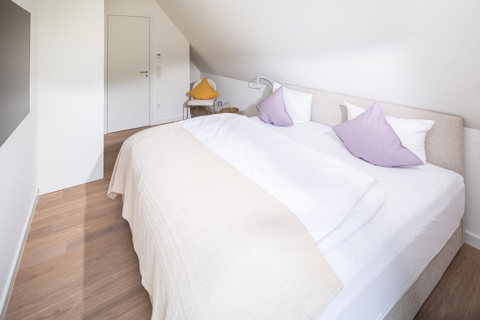 Schlafzimmer mit Doppelbett, Holzboden und schräger Decke.