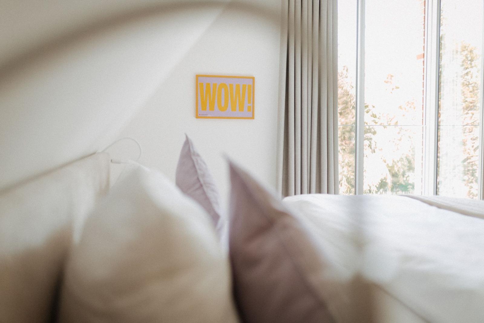 Schlafzimmer mit Bett, Wanddekoration und Fenster mit Blick auf Außenbereich.
